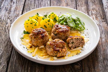 Seared pork meatballs with fried onion, boiled potatoes and lettuce in cream sauce on wooden table
