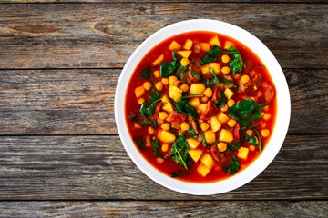 Delicious Spanish stew - chickpeas, spinach, seared chorizo, potatoes, tomatoes and broth on wooden table

