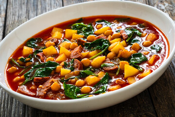 Delicious Spanish stew - chickpeas, spinach, seared chorizo, potatoes, tomatoes and broth on wooden table
