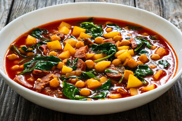 Delicious Spanish stew - chickpeas, spinach, seared chorizo, potatoes, tomatoes and broth on wooden table
