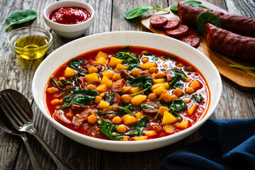 Delicious Spanish stew - chickpeas, spinach, seared chorizo, potatoes, tomatoes and broth on wooden table
