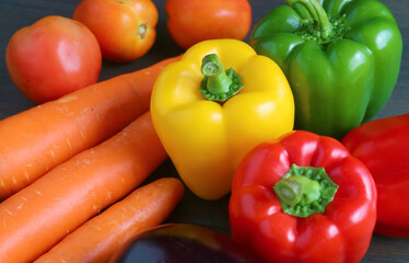 Closeup of yellow, red and green bell peppers with another fresh vegetables on wooden background