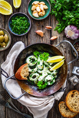Fried calamari rings with garlic, lemon and parsley in pan on wooden table
