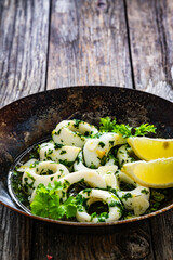 Fried calamari rings with garlic, lemon and parsley in pan on wooden table
