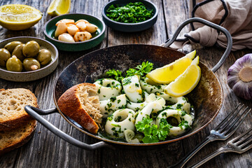 Fried calamari rings with garlic, lemon and parsley in pan on wooden table
