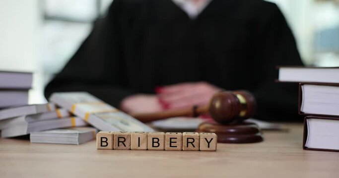 Word Bribery Made Of Wooden Cubes Against Female Judge Near Packs Of Money Cash And Gavel At Court Table. Fraud And Lawlessness In Law Enforcement