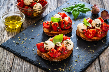 Tasty sandwiches - toasted bread with mozzarella balls cheese, tomatoes and basil leaves on wooden table
