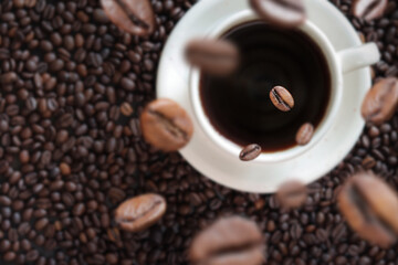 A cup of black coffee with scattered roasted coffee bean, top view. Americano coffee. Top view of a cup of coffee on the background of roasted coffee beans