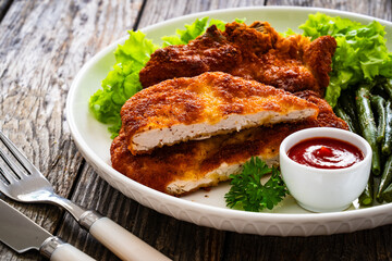 Breaded fried pork chop with cooked green beans on wooden table
