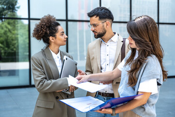 Fototapeta premium Team of business people talking in front of office building. Staff meeting quick briefing of office workers on motivational speech for employees. Businessman and businesswomen discussing opportunities