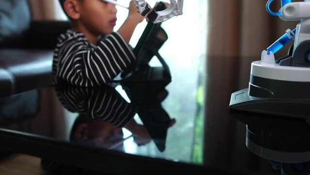 Boy asia constructs and programmes on computer and building a robot arm at home room