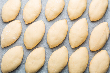 Fototapeta na wymiar Mini pies Pirozhki or piroshki, on a cooking tray ready to be baked. Homemade yeast boat shaped buns with cabbage fillings. Eastern Europe food background.