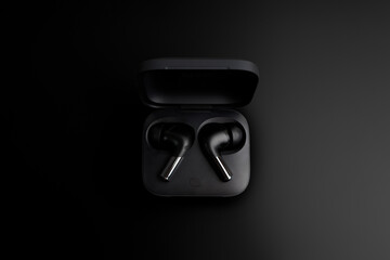 Closeup black TWS (true wireless stereo) earbuds in case isolated on black gradient background.