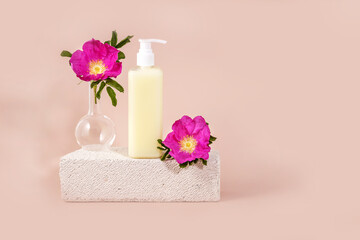 bottle pump and rosehip flowers in a laboratory flask on a podium made of stone on a beige background