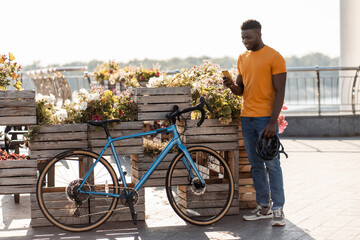 Portrait of handsome African American man holding mobile phone, standing near bicycle on street