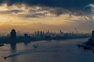Panoramic view over the Maas river in Rotterdam, the Netherlands during sunset and storm clouds with the silhouette of the port structures in the background