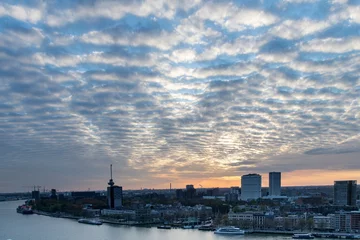Gordijnen Panoramic high level view during sunset over the Maas river and part of the city of Rotterdam, the Netherlands with cloudscape of cirrocumulus clouds coloring orange and yellow © Sonja