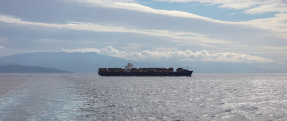 Container cargo ship full loaded is crossing open wavy sea at dusk. Import export, water transport.