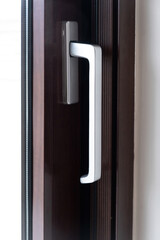Aluminum silver handle on close door, window against brown frame background. Close up view. Vertical