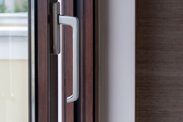 Aluminum silver handle on close window, door against brown frame background. Energy efficient.