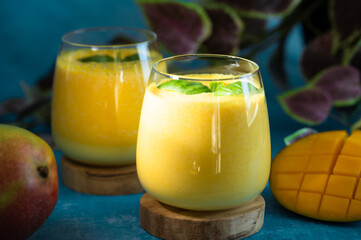Fresh mango lassi in glasses on blue background with copy space.