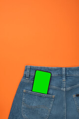 Smartphone mockup in back pocket of blue jeans on orange background. Banner with no people.