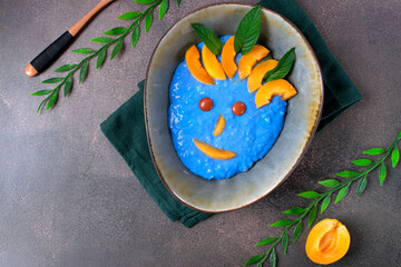 Blue rice porridge with spirulina and apricot in the ceramic bowl. Funny face. Healthy breakfast for kids. Top view