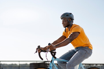 Authentic African rider wearing protective helmet and casual clothes riding bicycle, copy space