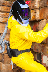 A man in a protective chemical suit and a welding mask on his head.