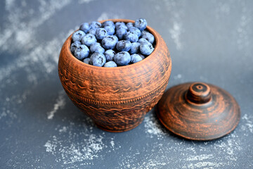 Ripe blueberries piled up in a clay, vintage pitcher, placed on a dark, gray background. Organic, nutritious food full of vitamins and minerals.