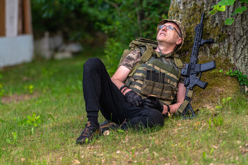 Naklejka na ściany i meble Armed man looking up while sitting under a tree