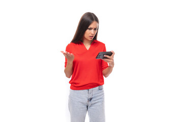 young caucasian female model with black straight hair dressed in a red t-shirt looks in surprise at a smartphone in her hands