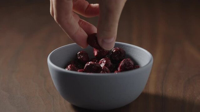 Slow motion freeze-dried cranberries taken by man hand from blue bowl on wood table with copy space