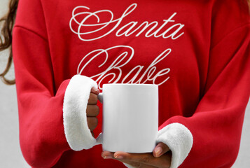 Girl is holding white 11 oz mug in hands with Christmas sweatshirt . Blank white ceramic cup