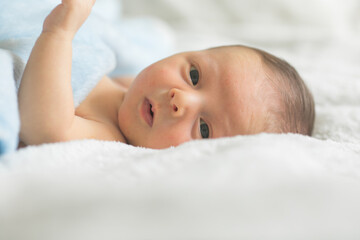 A cute newborn boy in the first days of life sleeps naked on a white fabric background.