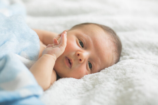 A cute newborn boy in the first days of life sleeps naked on a white fabric background.