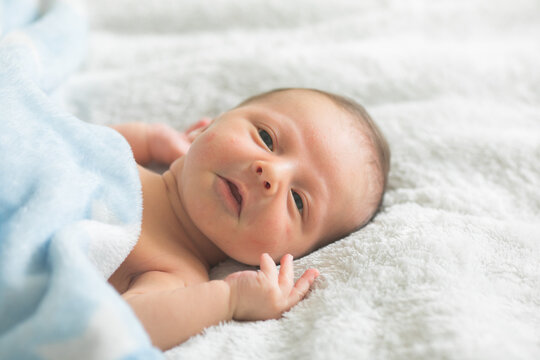 A cute newborn boy in the first days of life sleeps naked on a white fabric background.
