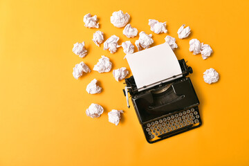 Vintage typewriter with a blank blank sheet and a pile of crumpled paper on a yellow background....