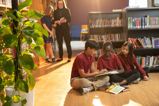 Elementary school students sitting in the library reading a book