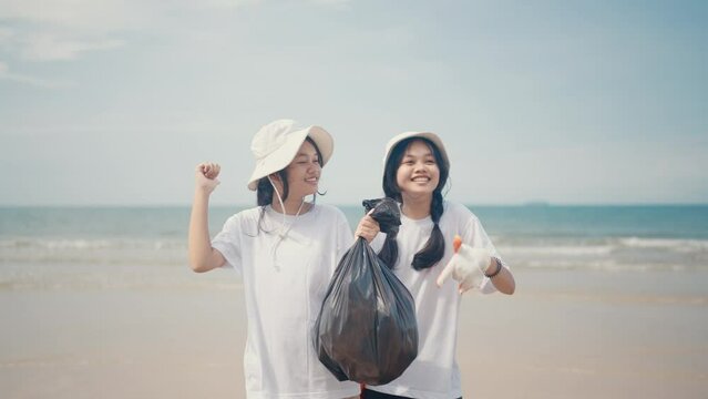 Two Asian girls holding black garbage bags on the beach Showing off the camera smiling happily.