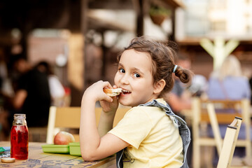 Cute little schoolgirl eating from lunch box outdoor sitting on a school cafe. Food for kids.