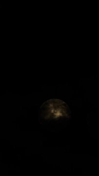 Detailed image of the full moon. Full moon against the black night sky. The clouds pass in front of the full moon. Vertical video for social media. 