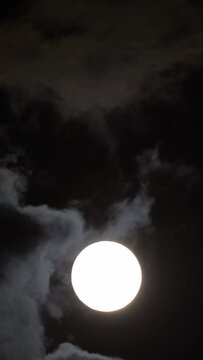 Detailed image of the full moon. Full moon against the black night sky. The clouds pass in front of the full moon. Vertical video for social media. 