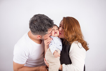 Beautiful photo of Dad and mom being affectionate with baby on light photo studio background. Family and baby concept.