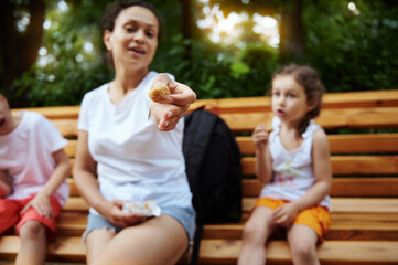 Focus on a dried figs fruit in the hands of a smiling woman, cheerful mother chilling out with her kids in the city park