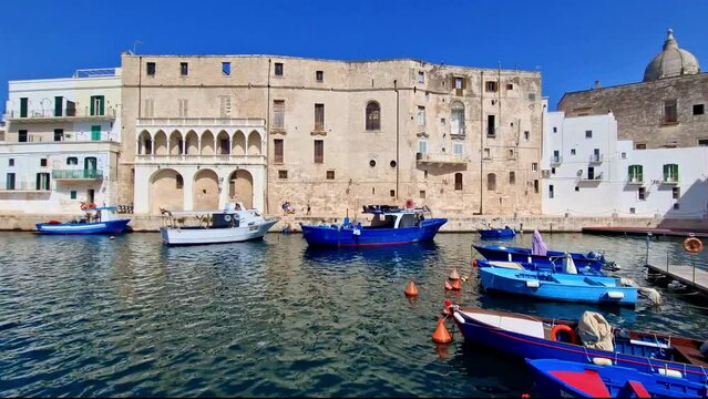 Monopoli white town view in Puglia Italy with colorful traditional fishing boats. Beautiful scenic old seaport harbor and blue Mediterranean sea water at sunny summer day. Travel footage 4k