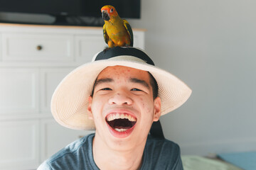 Confidente teenage boy wearing red cap with big smile, joy face and his pet,Sun Conure on his head,Animals therapy for person with special need,Hobby,Rehabilitation friendship of best friends concept.