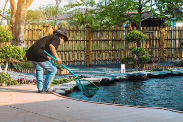 Back view of Asian woman in a black hat and black shirt wearing jeans using dip-net to scoop up...