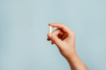 White pill in female hand on blue background, Taking Your Medication - obrazy, fototapety, plakaty