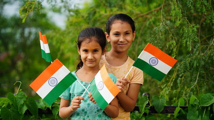 Two Indian child celebrating Independence or Republic day, Cute little Indian child holding, waving with Tricolour flag with greenery in the background.